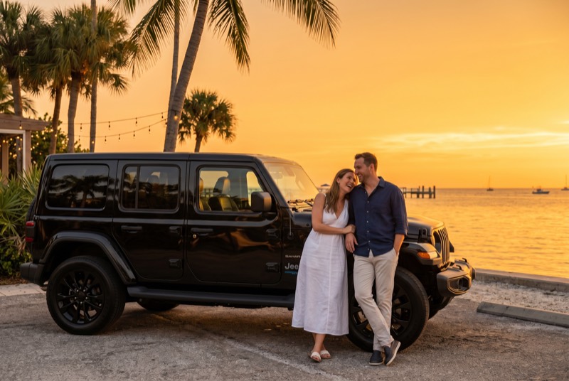 Couple at a Naples waterfront overlook at sunset with a black Jeep Sahara